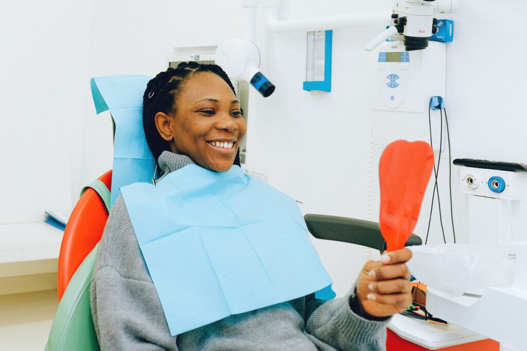 Woman in a dentist's chair holding a hand mirror admiring the results of a clear aligner lab